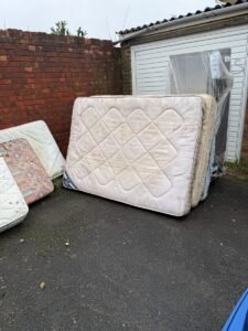 Old double mattresses stacked outside a garage awaiting mattress disposal in Kent