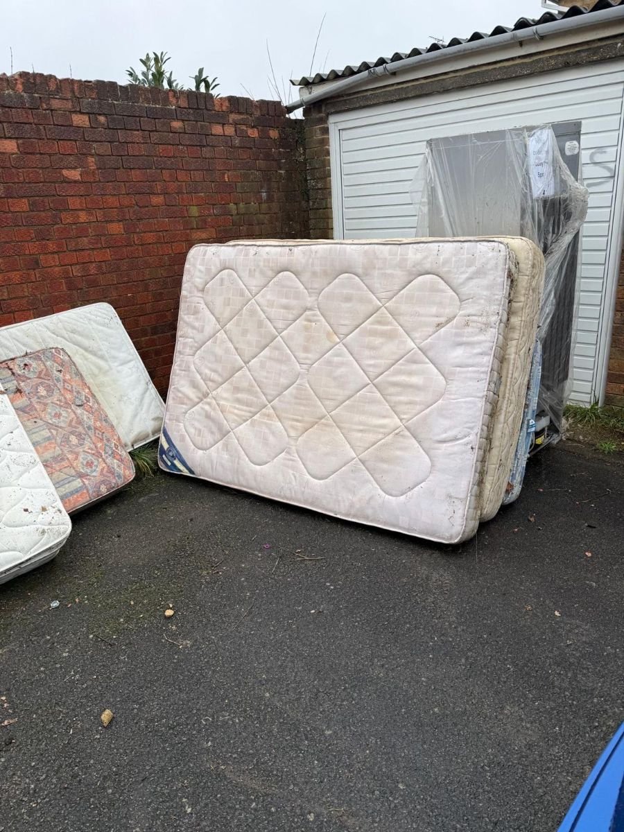 Old double mattresses stacked outside a garage awaiting mattress disposal in Kent
