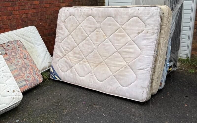 Old double mattresses stacked outside a garage awaiting mattress disposal in Kent